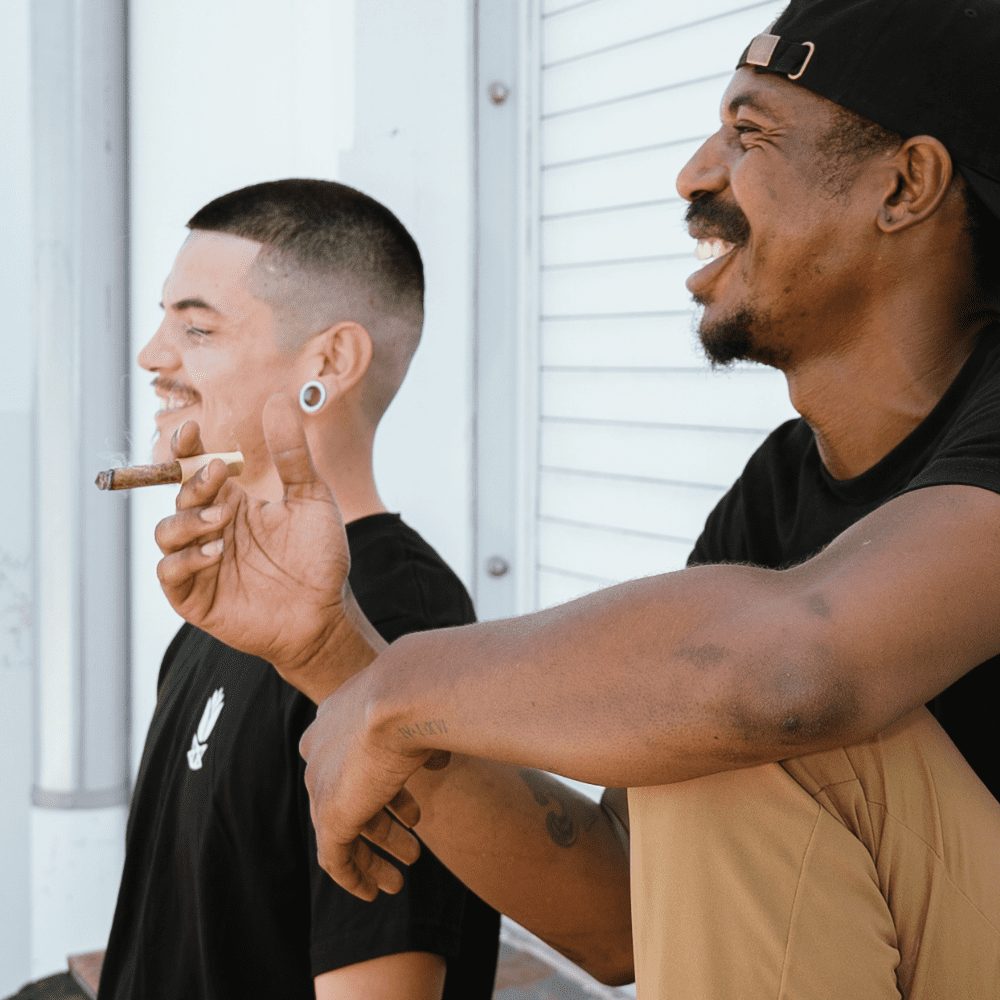 Two men smiling and smoking a blunt outdoors created with cannagar press and wrapped with a Native Leaf Co. hemp wrap